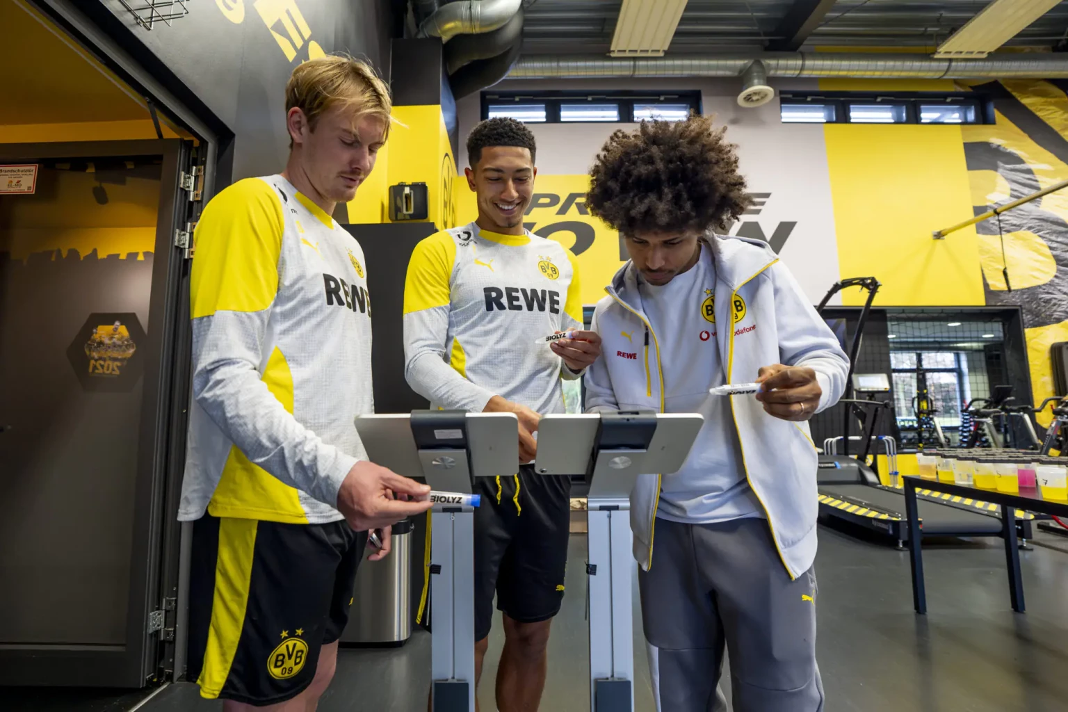 Die BVB-Spieler Jobe Bellingham, Julian Brandt und Karim Adeyemi mit Biolyz-Testkits | (c) Borussia Dortmund